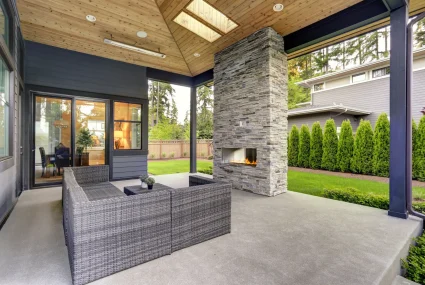 New modern home features a backyard with covered patio accented with stone fireplace, vaulted ceiling with skylights and furnished with gray wicker sofa placed on concrete floor. Northwest, USA